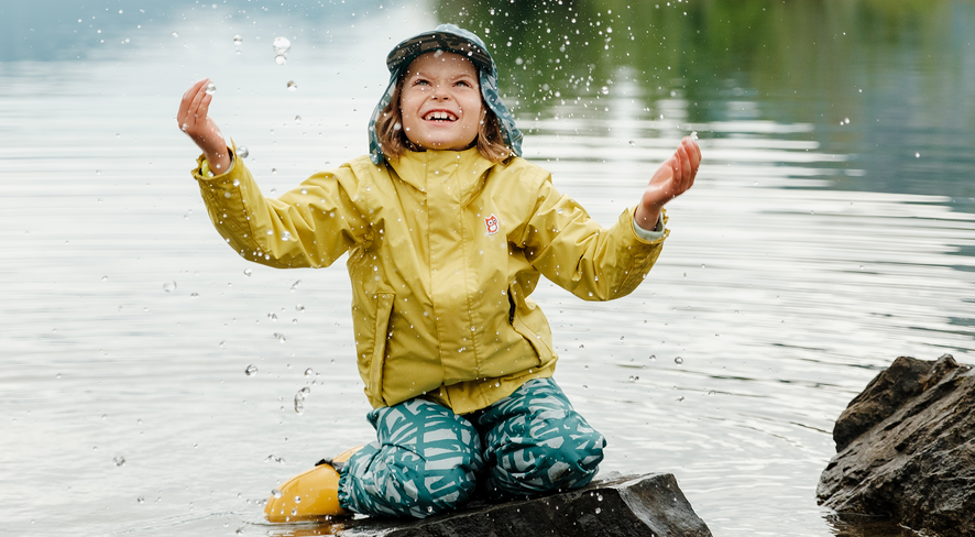 child playing in the water with rain gear on