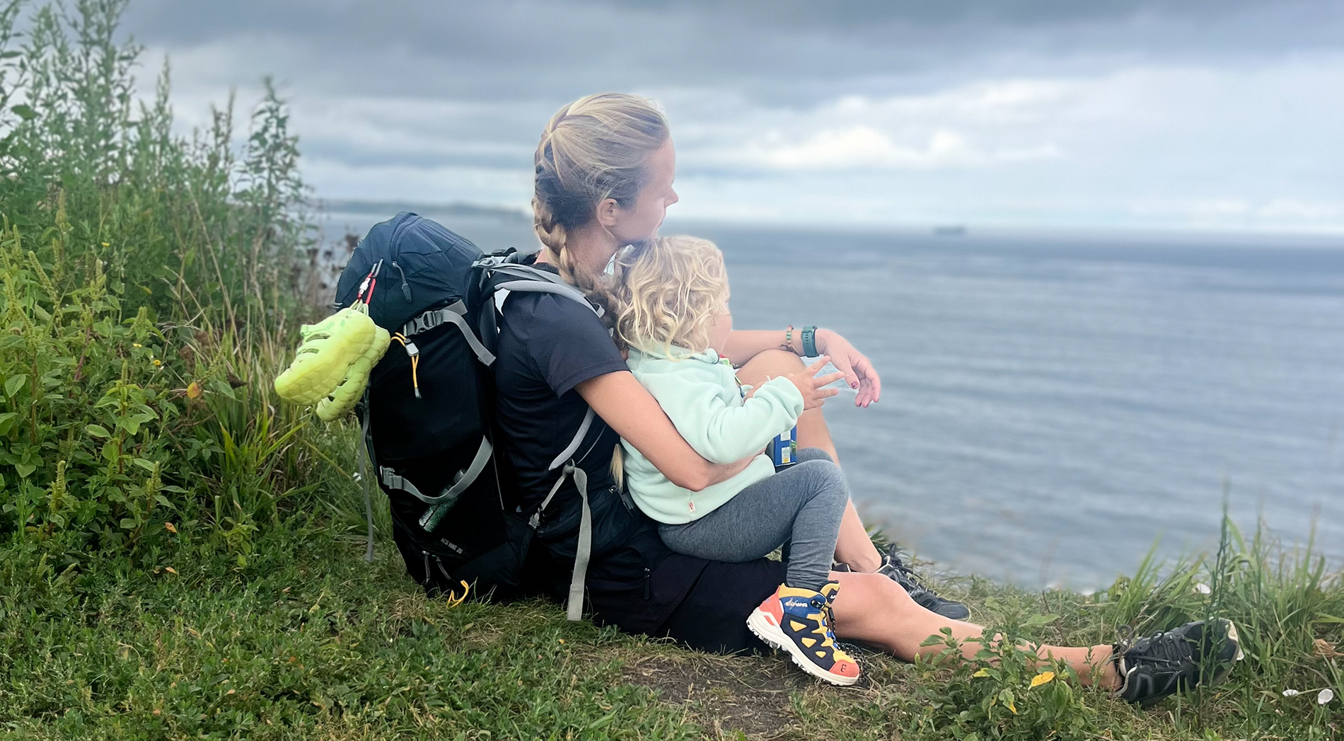 A mother and kid in namuk clothes sitting on a hill looking out at the sea